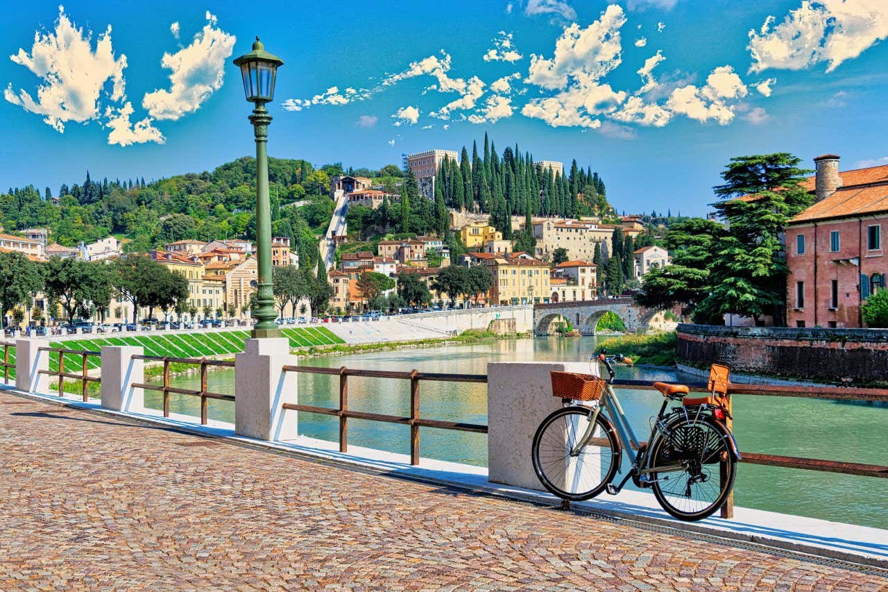A bike leaning against a railing next to a river, with views of hills under a blue sky with white clouds.