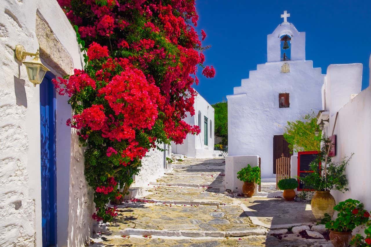 Uma viela típica na ilha grega de Amorgos, com casas e uma pequena igreja branca sob um céu azul