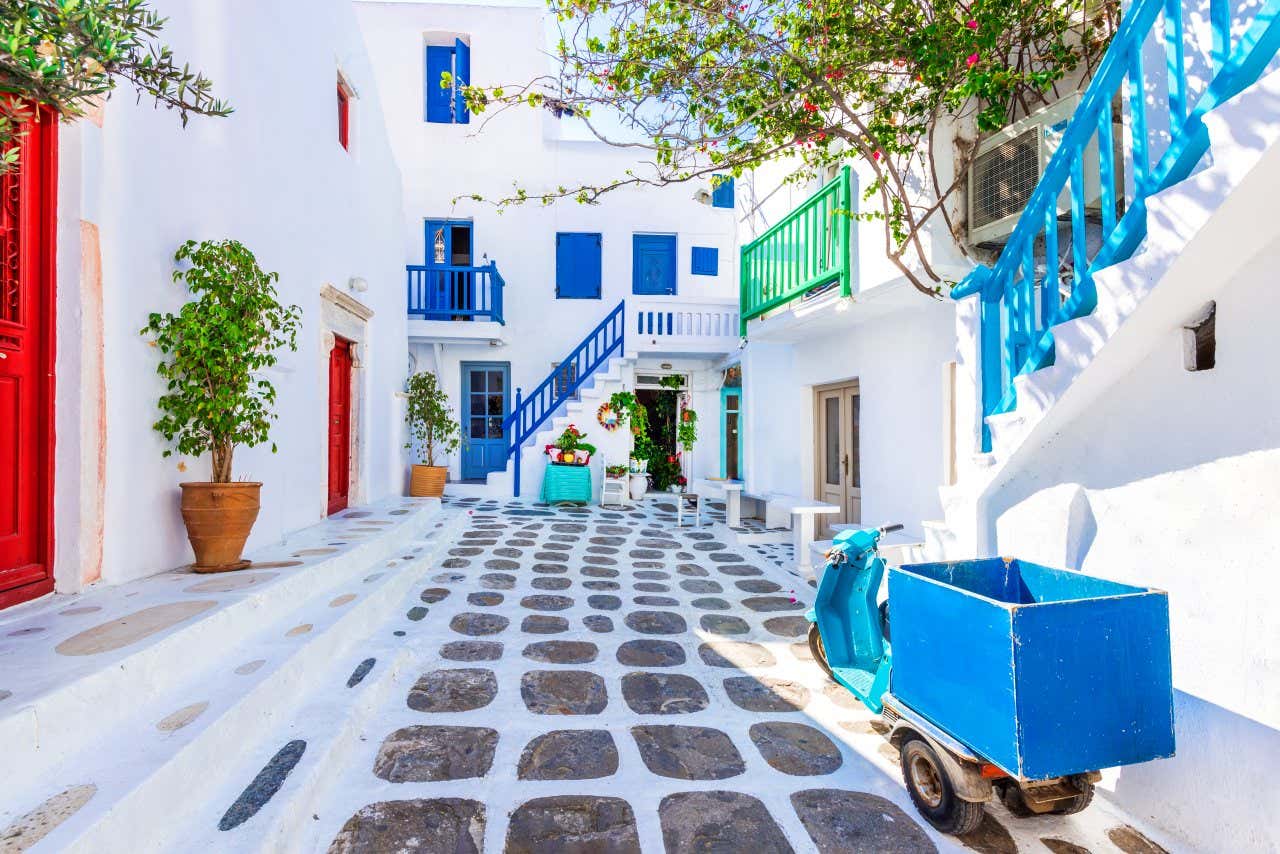 Uma viela com casas brancas e detalhes coloridos, na ilha grega de Mykonos