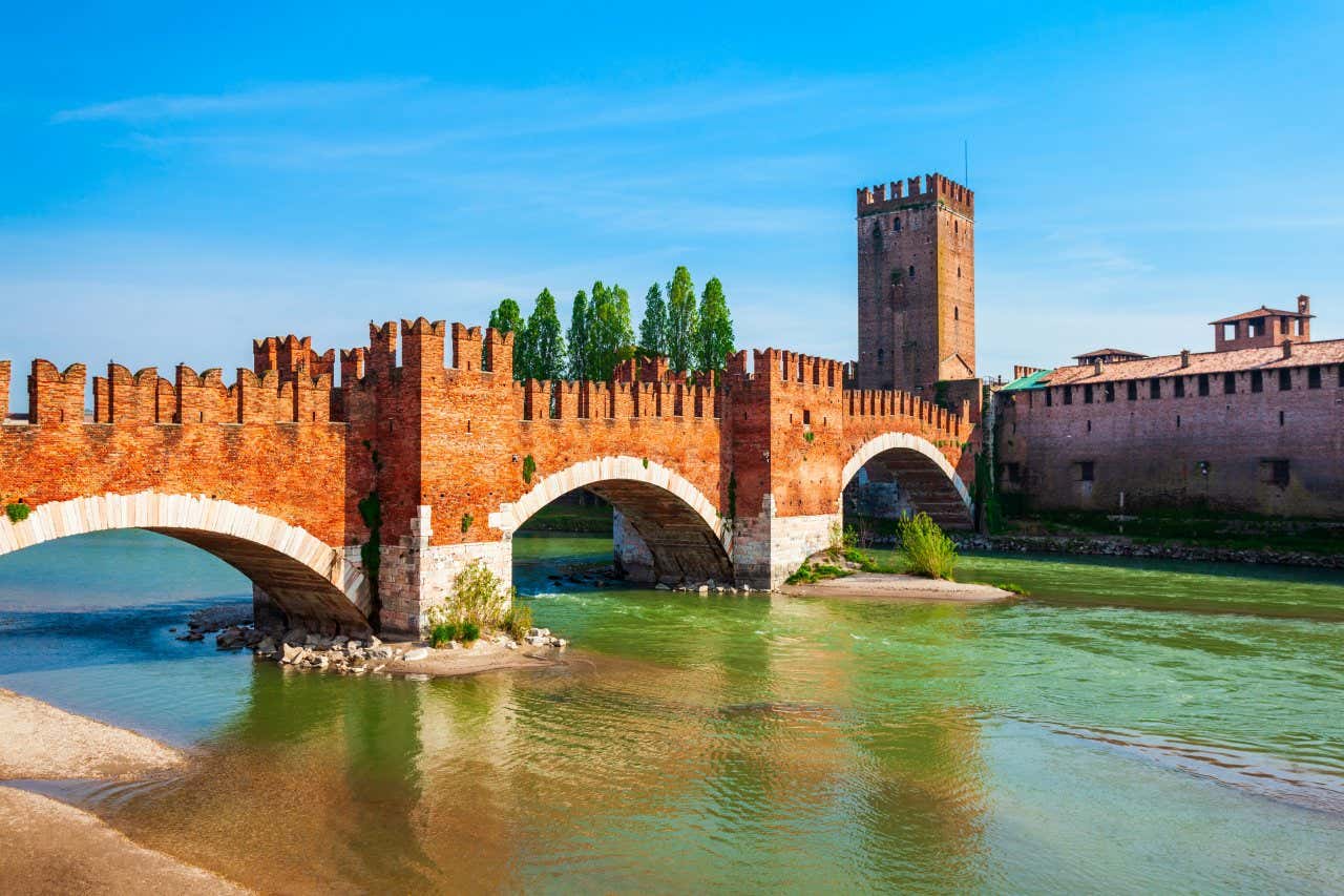 A view of Castelvecchio and the bridge leading to it from across the water under a blue sky