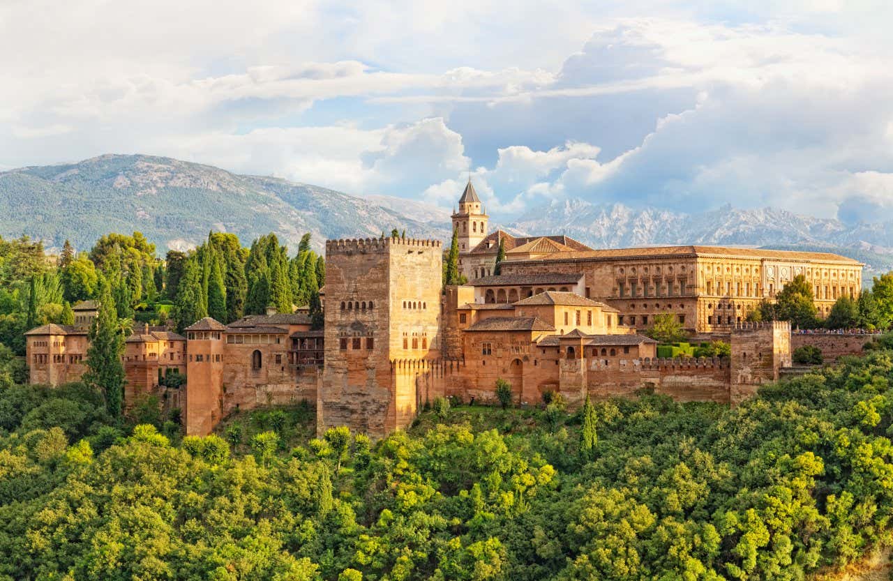 Panoramica dell'Alhambra, circondata da vegetazione con le montagne e il cielo nuvoloso sullo sfondo