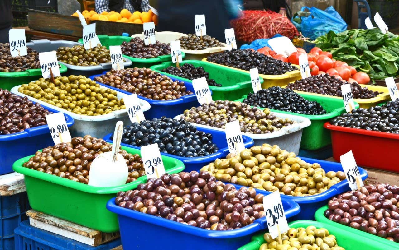 Several colourful buckets of fresh produce such as Olives and prices tags on top of them 