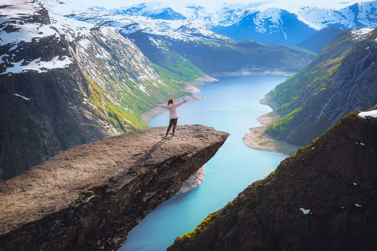 Femme sur un énorme rocher surplombant un lac et des montagnes enneigées