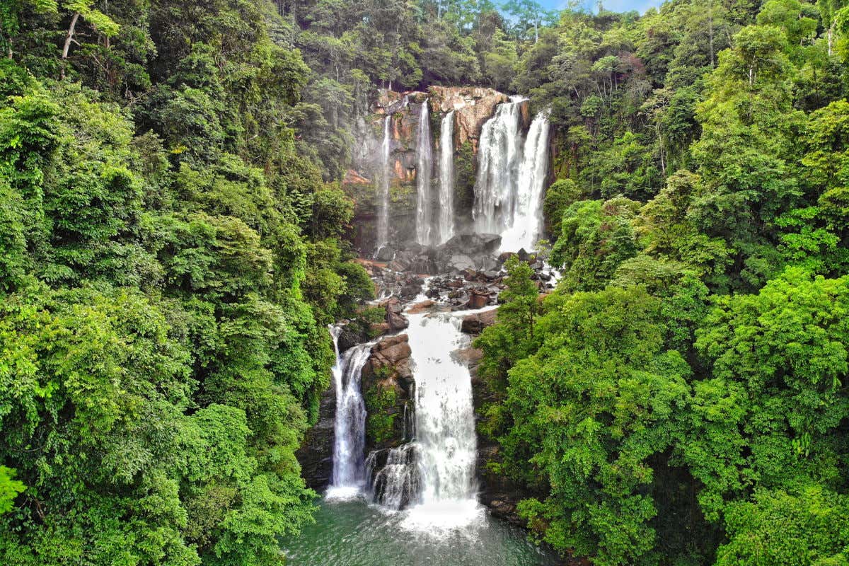 Una cascada cayendo en tres niveles de altura hacia un manantial en mitad de una frondosa selva de Costa Rica