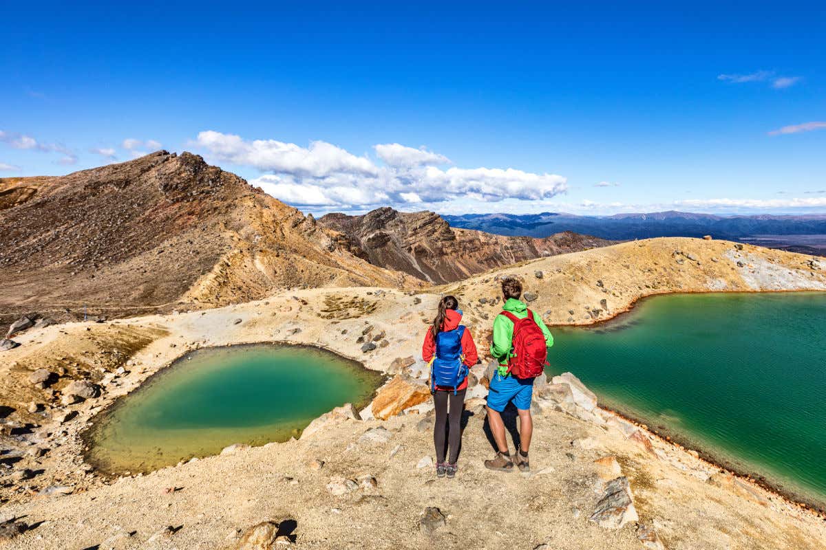 Una pareja practicando senderismo en Nueva Zelanda entre manantiales y paisajes montañosos en un día parcialmente nuboso