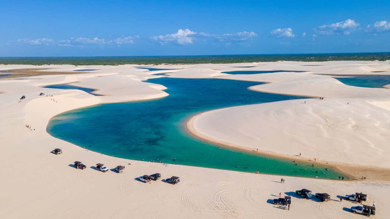 Vista aérea das dunas de Lençóis Maranhenses com as lagoas turquesas entre elas e diversos jipes e turistas   