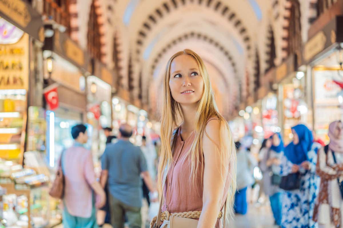 Una mujer rubia posando ante la cámara en un pasillo repleto de arcos y puestos de venta en el Gran Bazar de Estambul