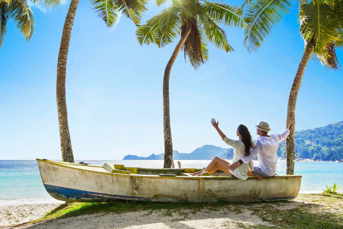 Una pareja subida en un barco en la arena de una playa y junto a varias palmeras