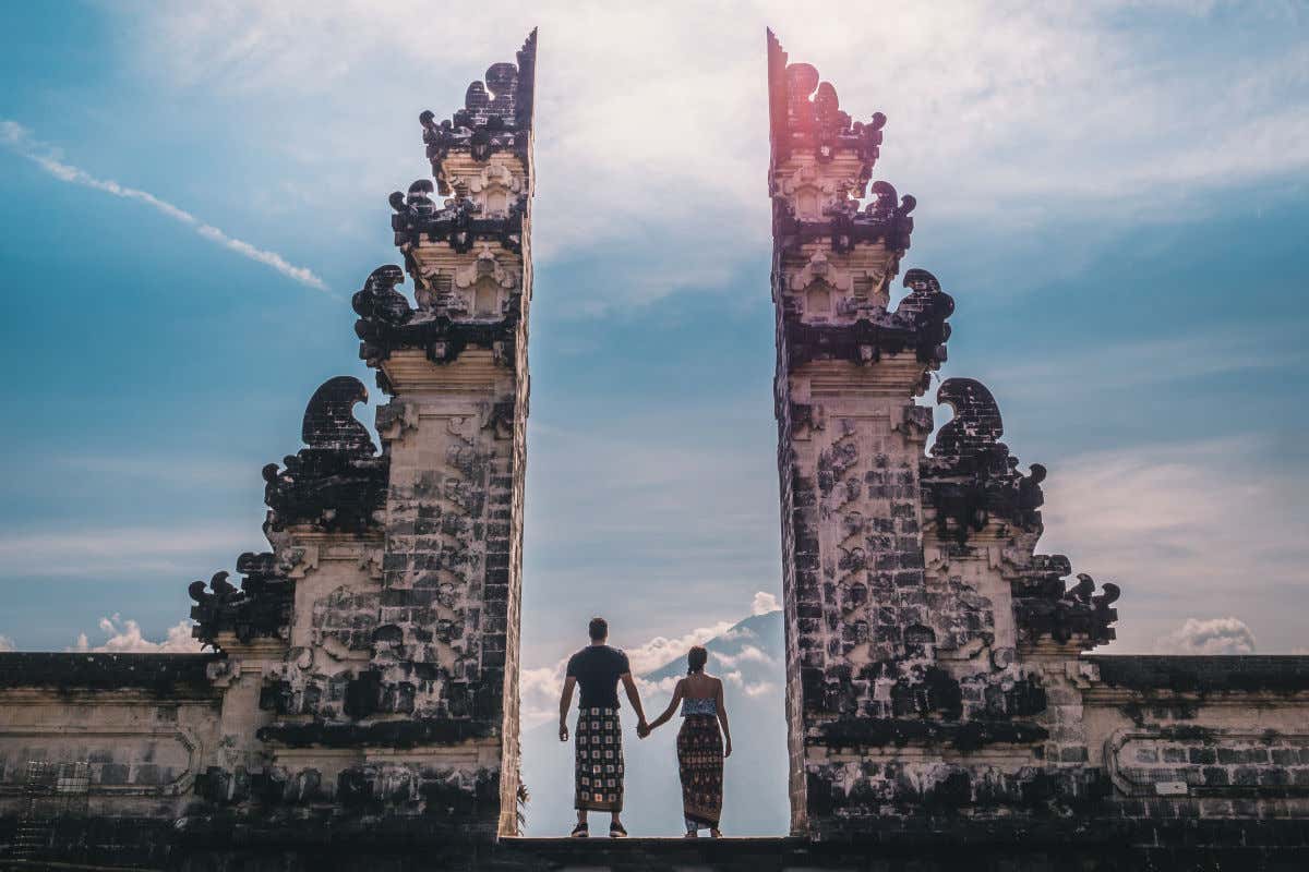 Una pareja de espaldas entre dos enormes columnas de piedra pertenecientes al templo Lempuyang de Bali