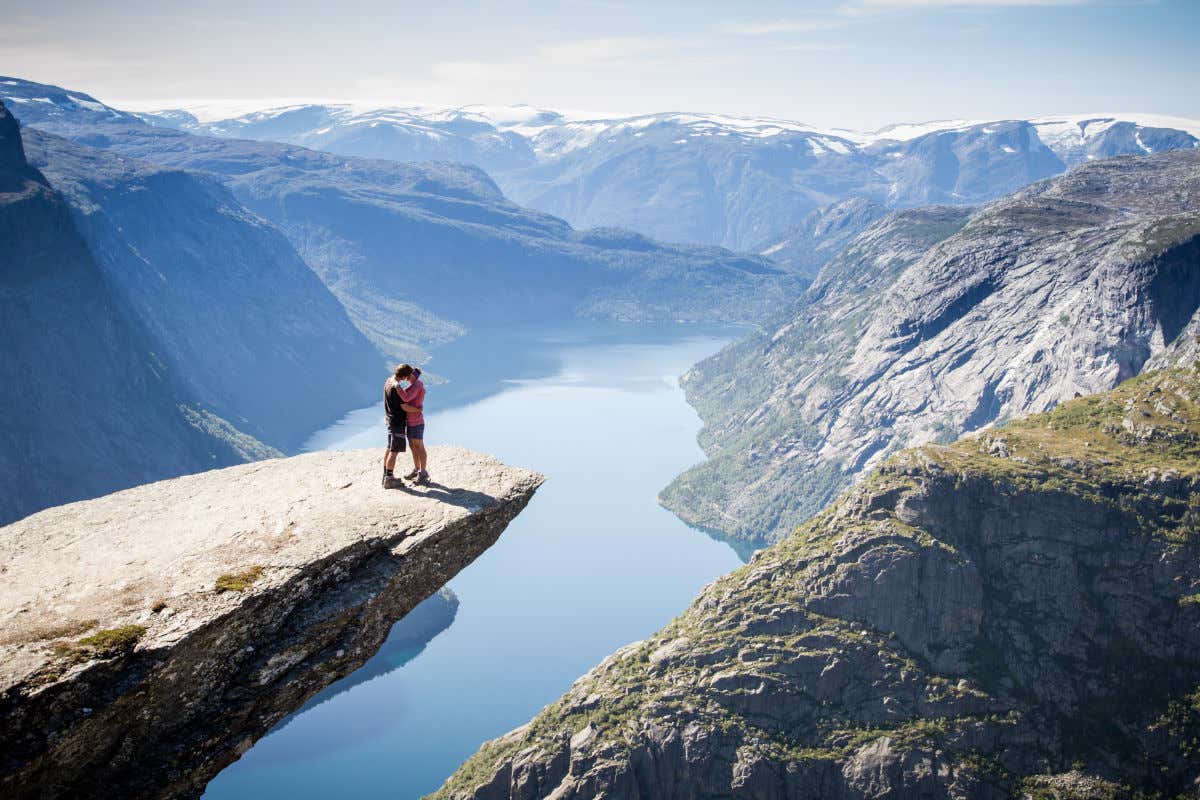 Una pareja besándose en una roca aislada y situada a gran altura sobre los fiordos noruegos
