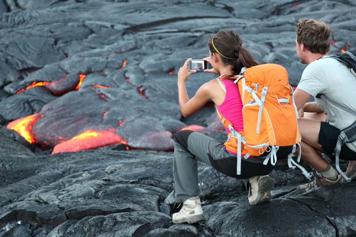 Una pareja de senderistas fotografiando una colada de lava de aspecto negruzco y rojizo