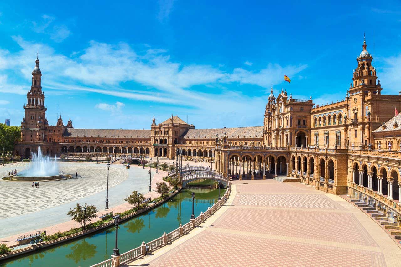 A view of Plaza de España, Seville, on a sunny day with a few people walking around near the fountain.
