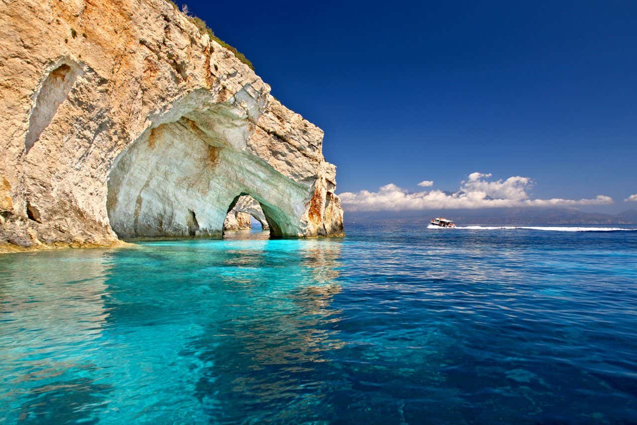 Un arco di roccia naturale si tuffa nel mare turchese e sullo sfondo un motoscafo