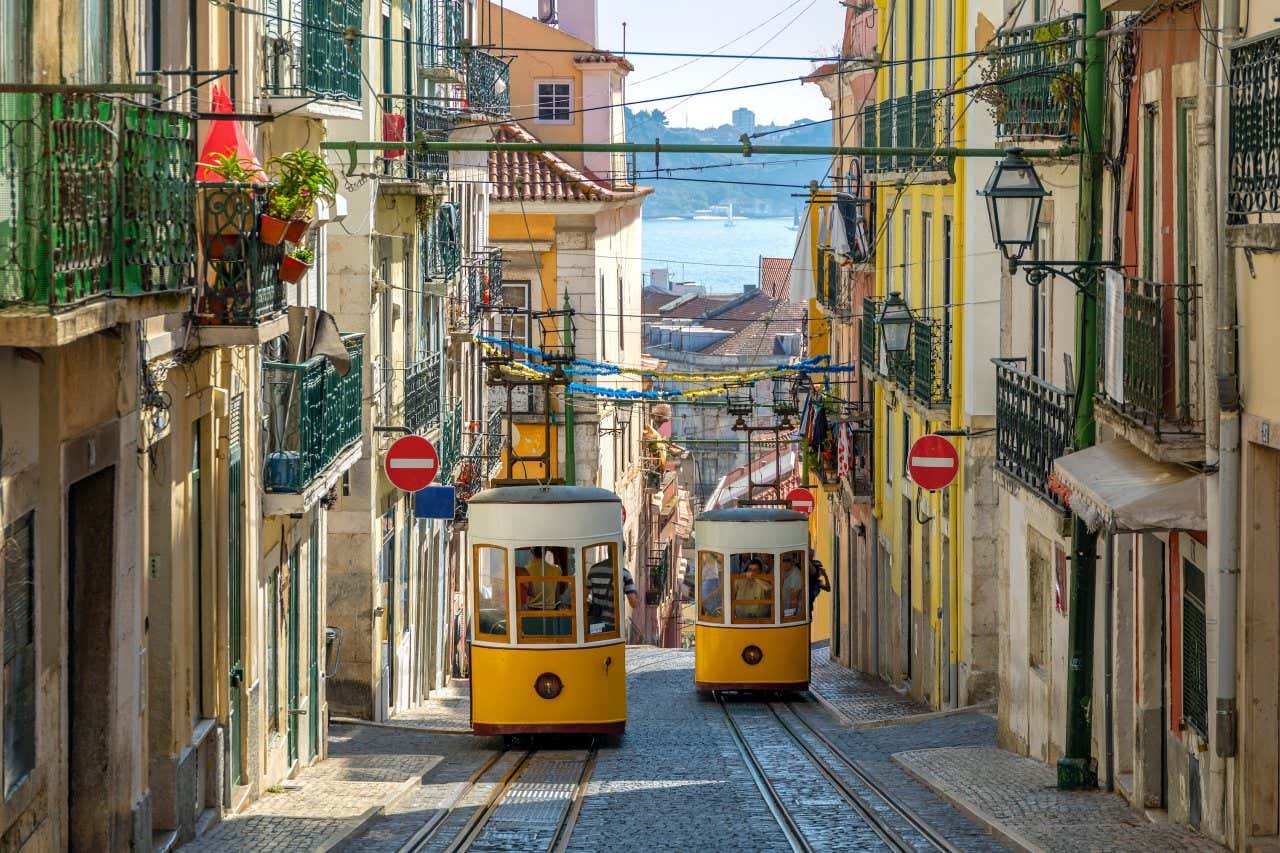 Dois funiculares descendo uma estreita rua de pedra com casinhas coloridas ao lado