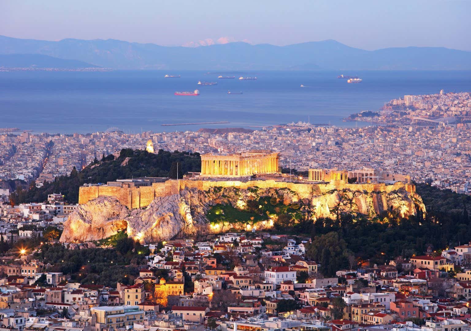 Panoramica sull'Acropoli di Atene che domina la città con i suoi templi illuminati di sera e circondata dalle case della capitale greca