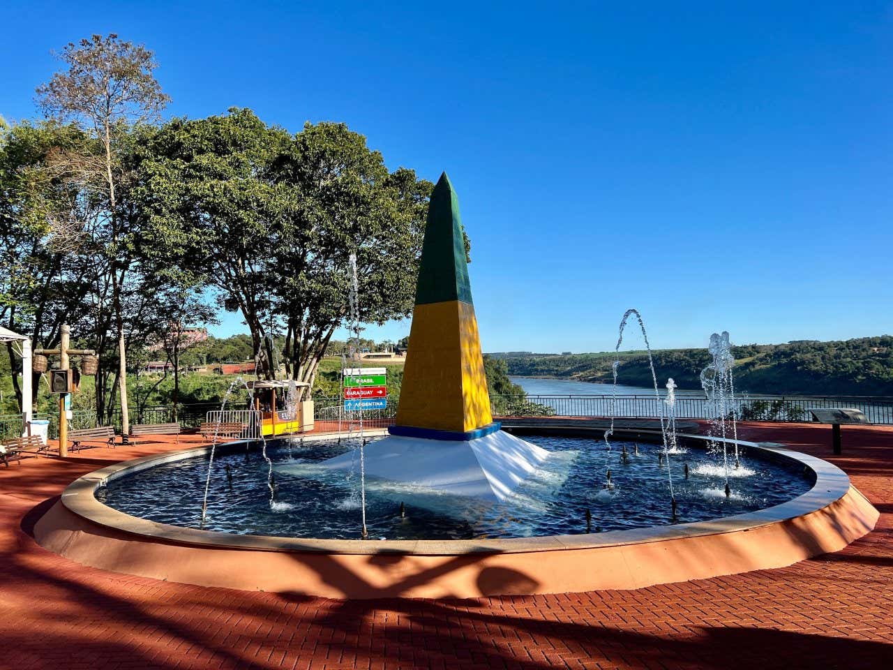 Monumento brasileiro do Marco das Três Fronteiras pintado de verde e amarelo no centro de uma fonte. 