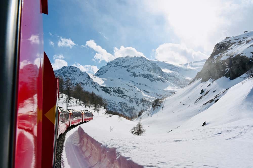 Paesaggio alpino innevato fotografato dal finestrino di un treno svizzero in una giornata di sole