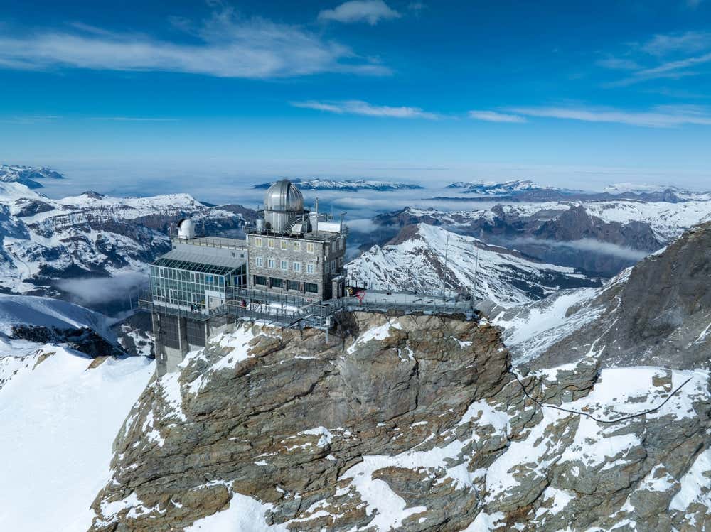 Un edificio in metallo incastonato sulla cima di un monte svizzero, tra cime innevate e ghiacciai
