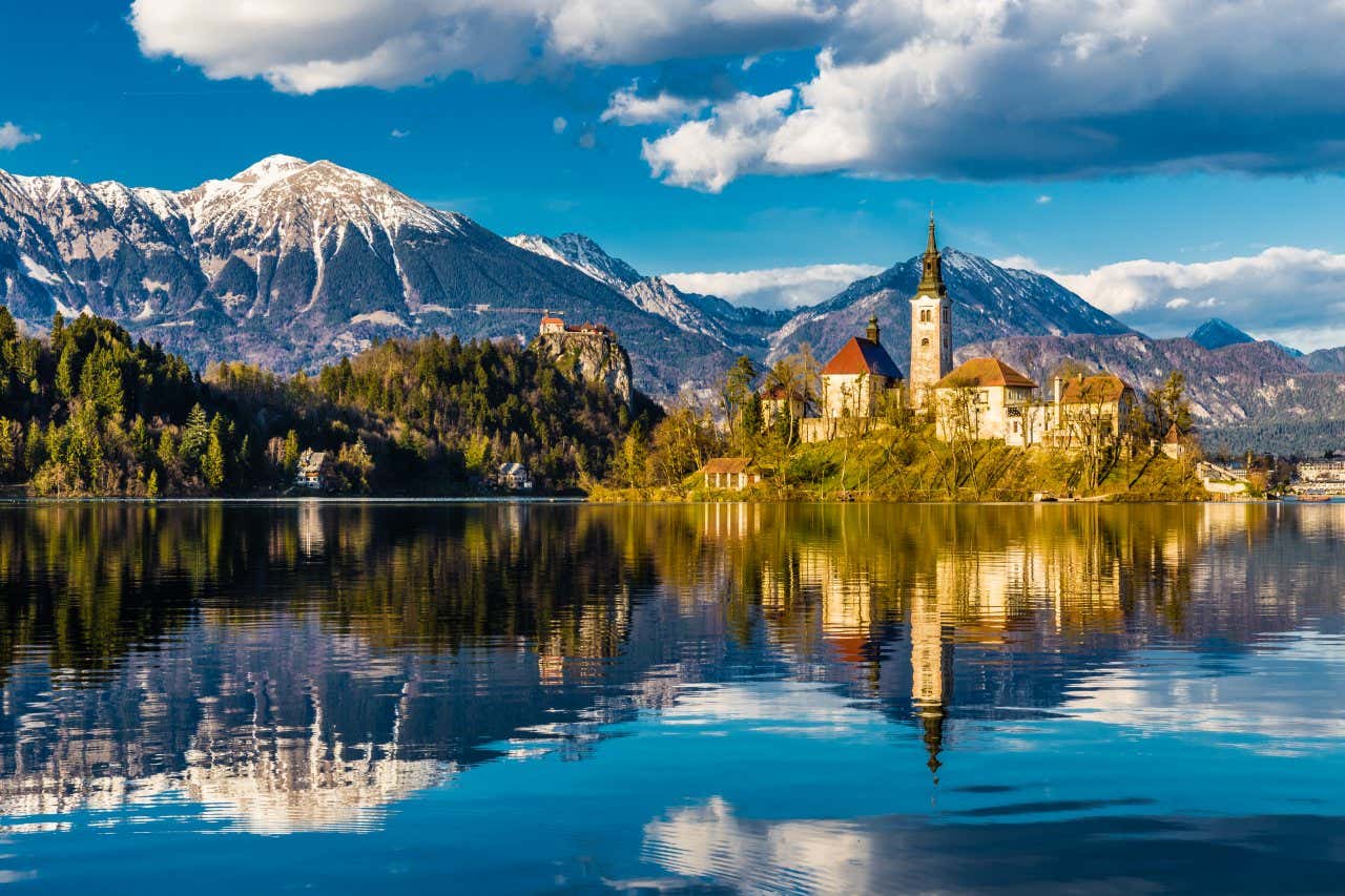 Una chiesa con campanile su un'isola al centro di un lago con montagne sullo sfondo
