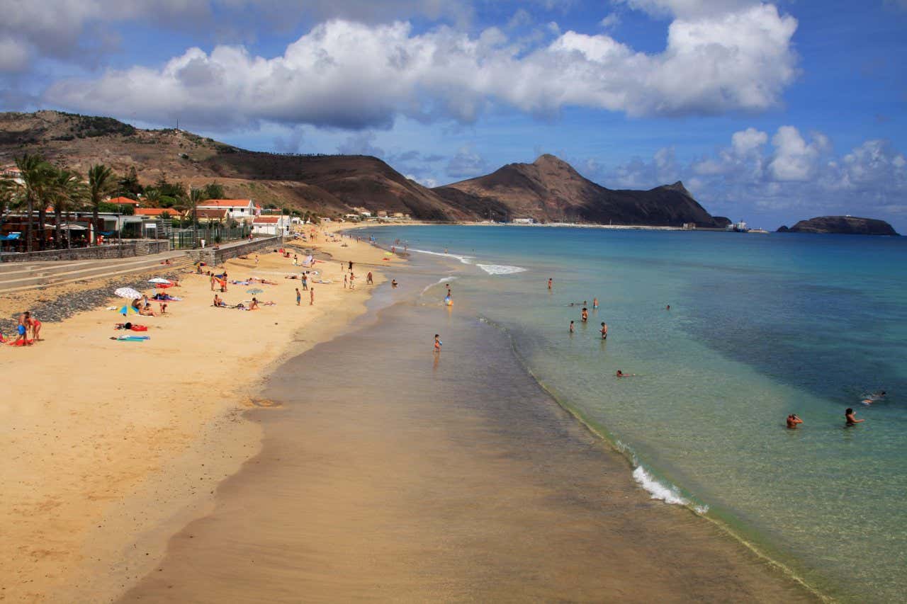 Alcuni bagnanti prendono il sole e altri fanno il bagno in una spiaggia con alcune montagne sullo sfondo