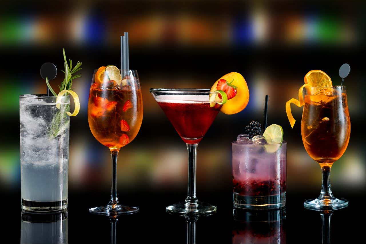 Diversi bicchieri pieni di miscele alcoliche colorate ornati con agrumi e frutta