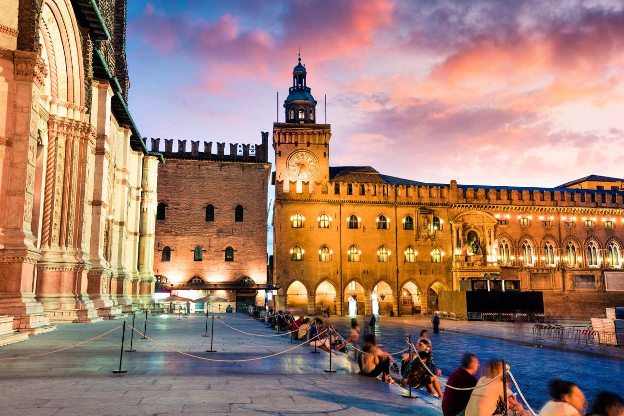La piazza centrale di Bologna di sera con diverse persone che riposano sugli scalini di pietra bianca