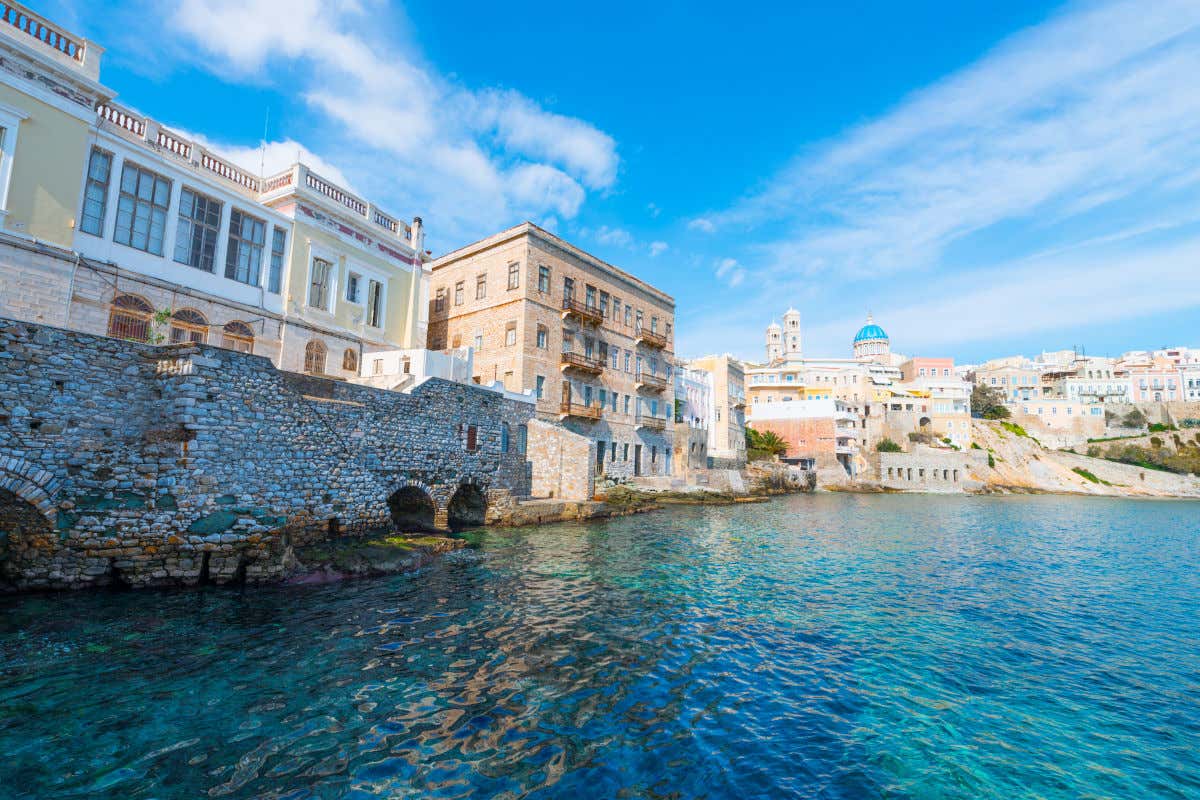 Aguas cristalinas junto a varios edificios y una catedral en primera línea del mar en la isla griega de Siros