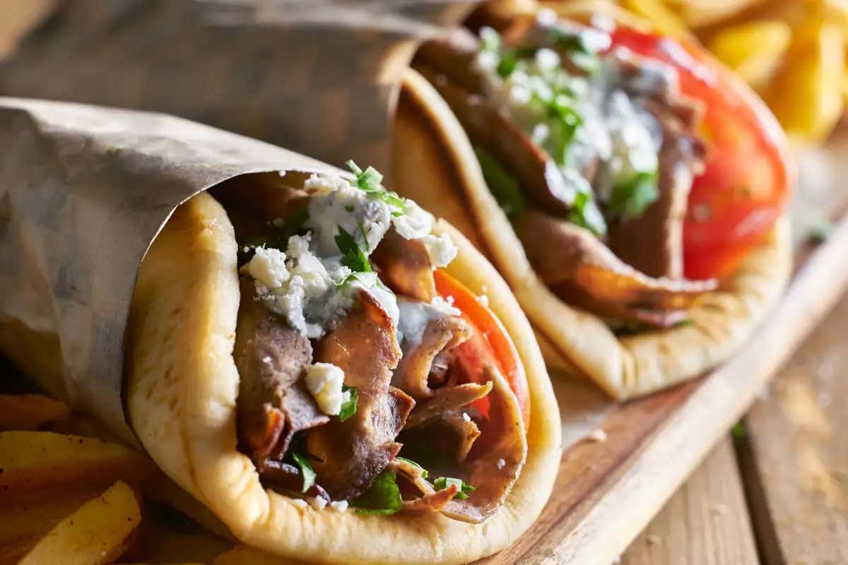 Dois gyros recheados de carne bovina embrulhados em papel pardo sobre uma mesa de madeira