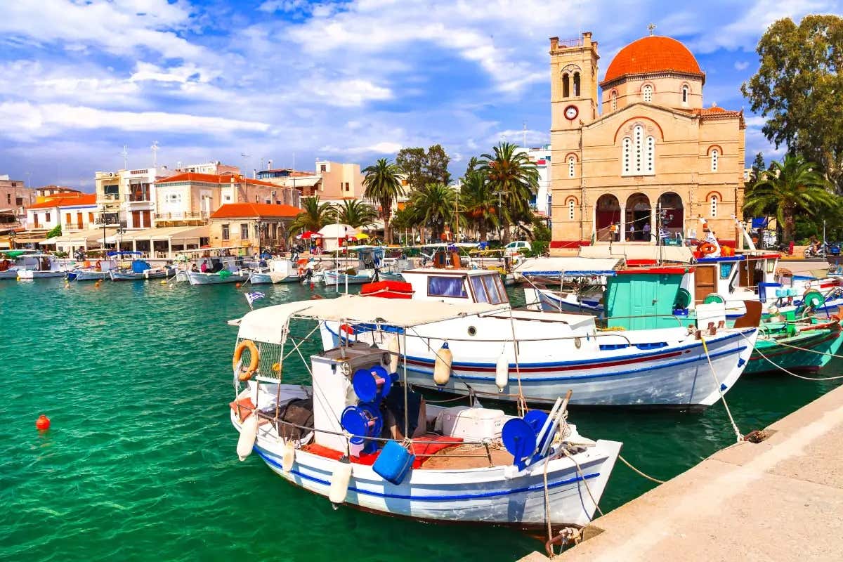 Porto repleto de barcos boiando em águas verdes com edifícios gregos ao fundo