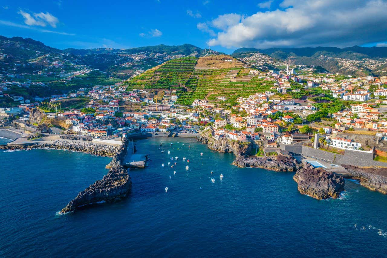 An aerial view of Funchal's coastline with several boats in the bay under a blue sky with some clouds.
