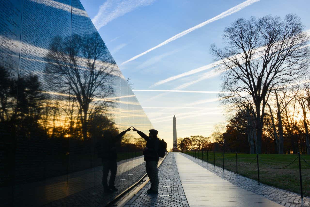 Un uomo in controluce indica un nome sul Muro dei Veterani del Vietnam