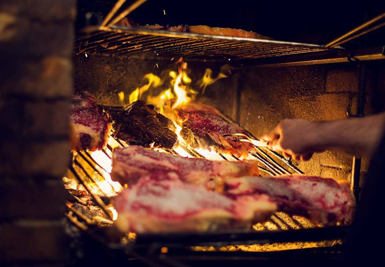 Un hombre moviendo unos cortes de carne en la parrilla