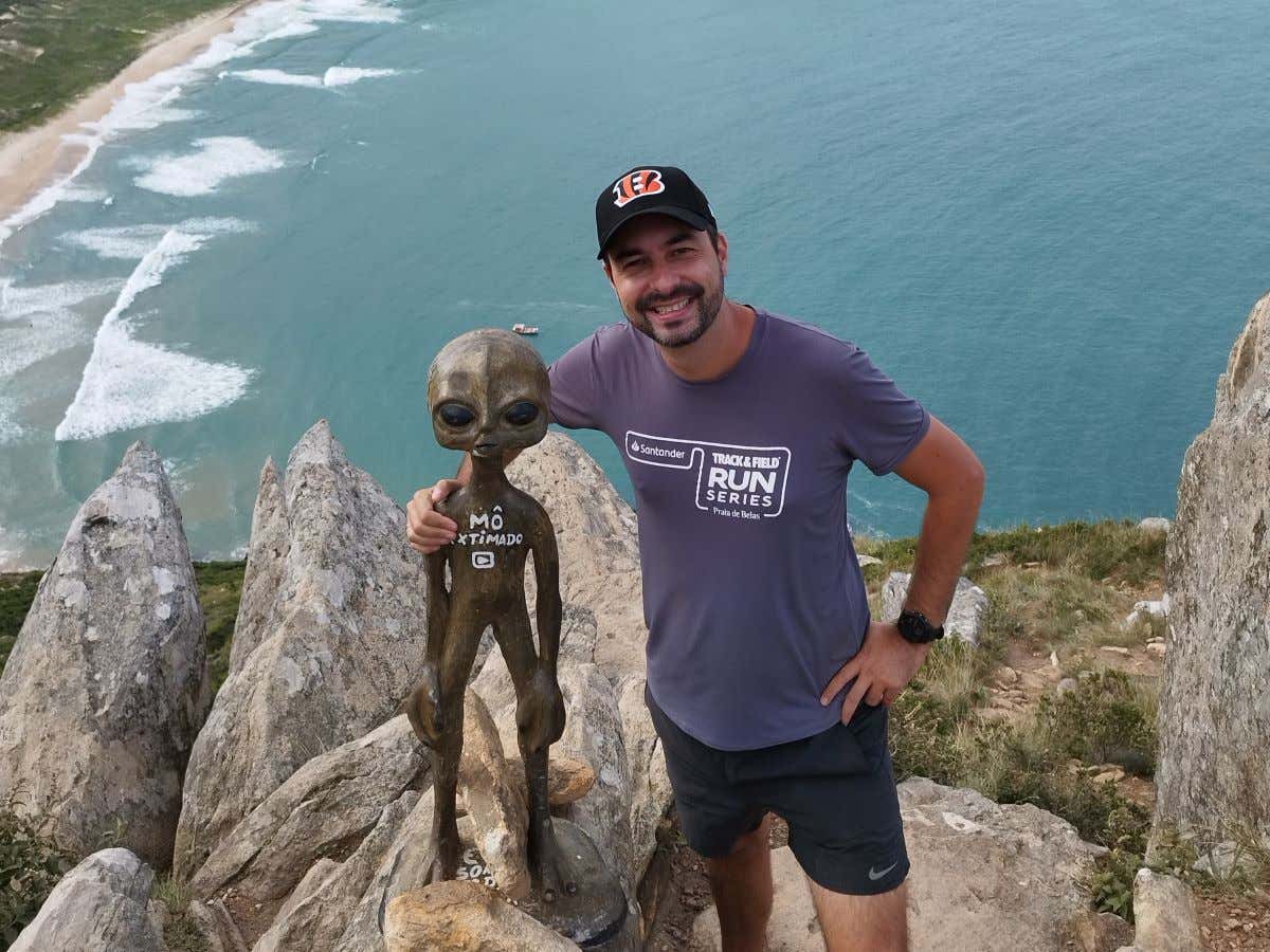 Un joven sonriendo al lado una estatua de un extraterrestre en un mirador al mar