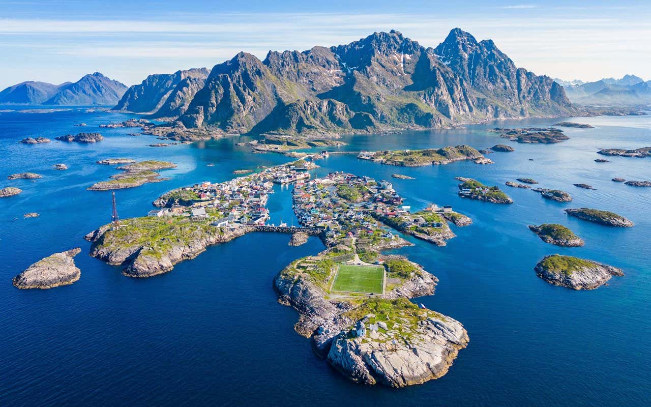Vue panoramique sur des îlots des Îles Lofoten avec un terrain de foot au premier plan et une montagne en fond