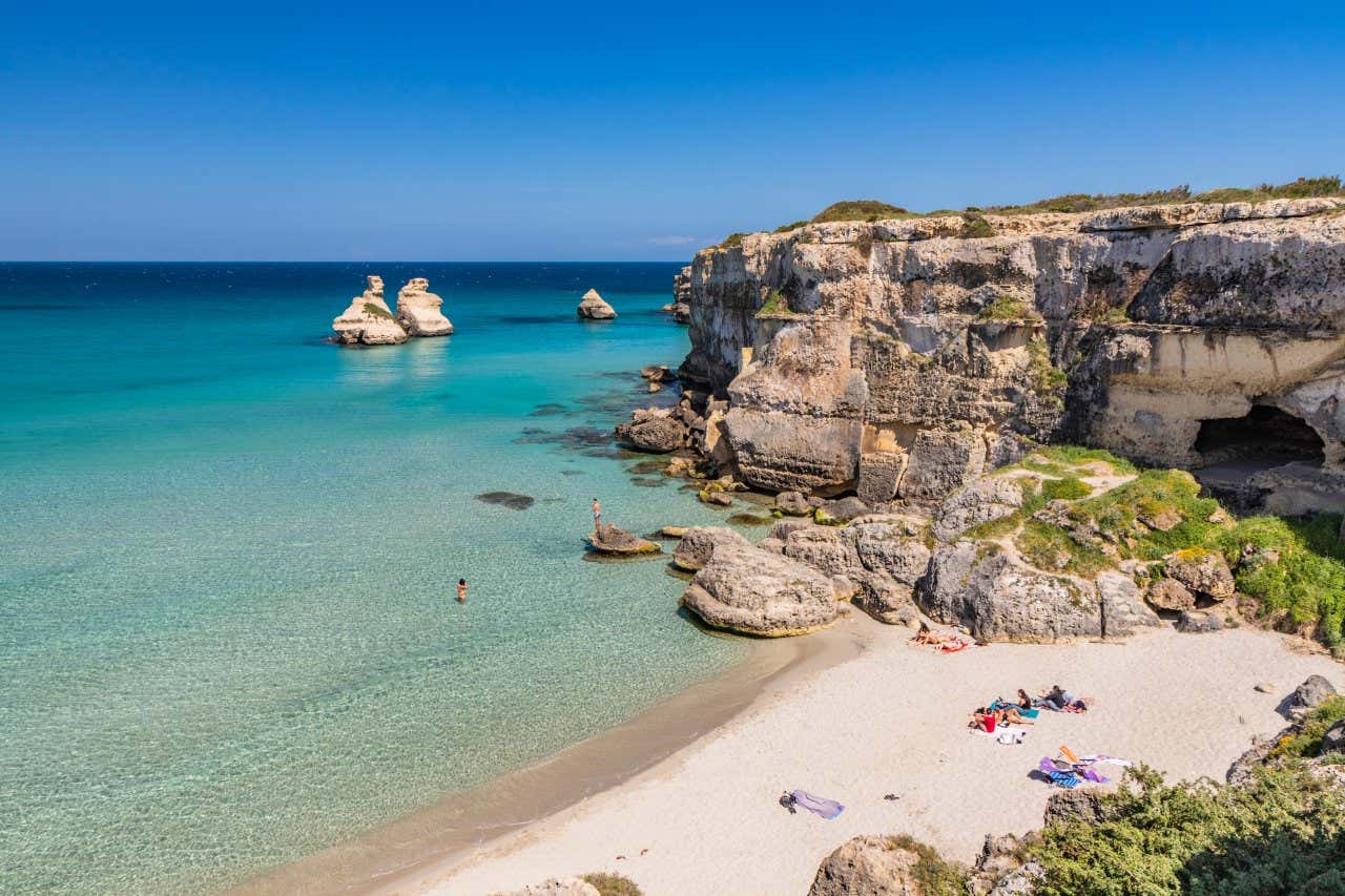 Una spiaggia del Salento con acqua cristallina, scogli e poche persone sdraiate sul bagnasciuga
