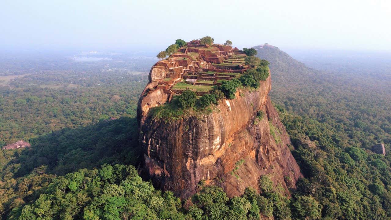 Una formazione rocciosa tondeggiante emerge da una foresta e in cima ci sono i resti di un'antica città dello Sri Lanka