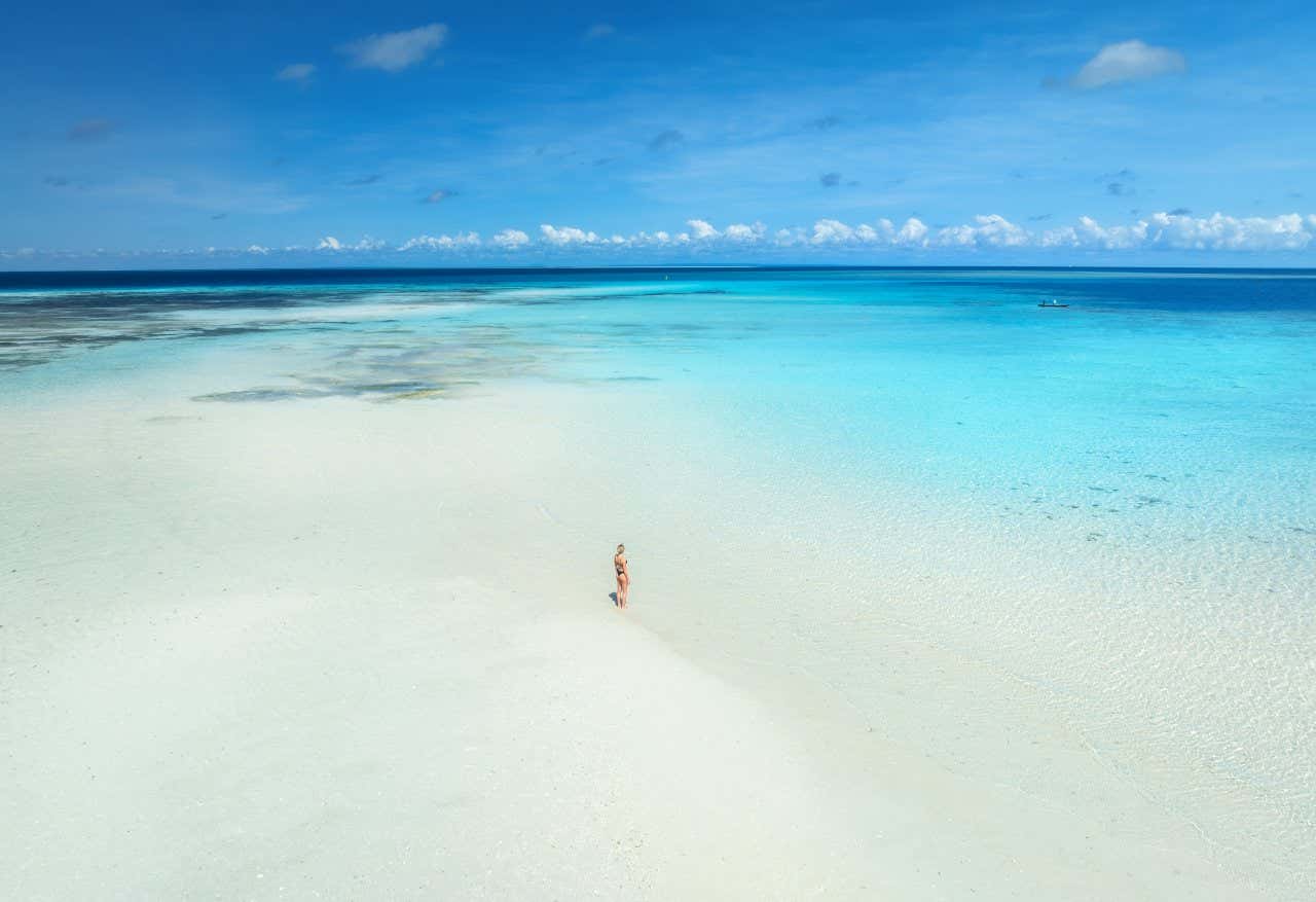 Una donna in mezzo a una vasta spiaggia di sabbia bianca circondata dal mare turchese dello Zanzibar