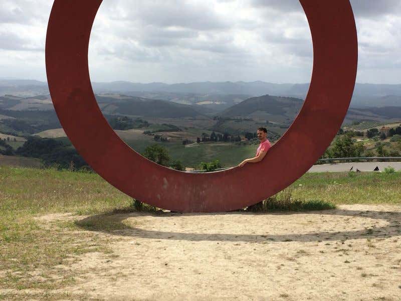 Francisco Alcón haciéndose una foto a través de una estructura en forma de círculo con las montañas de Toscana