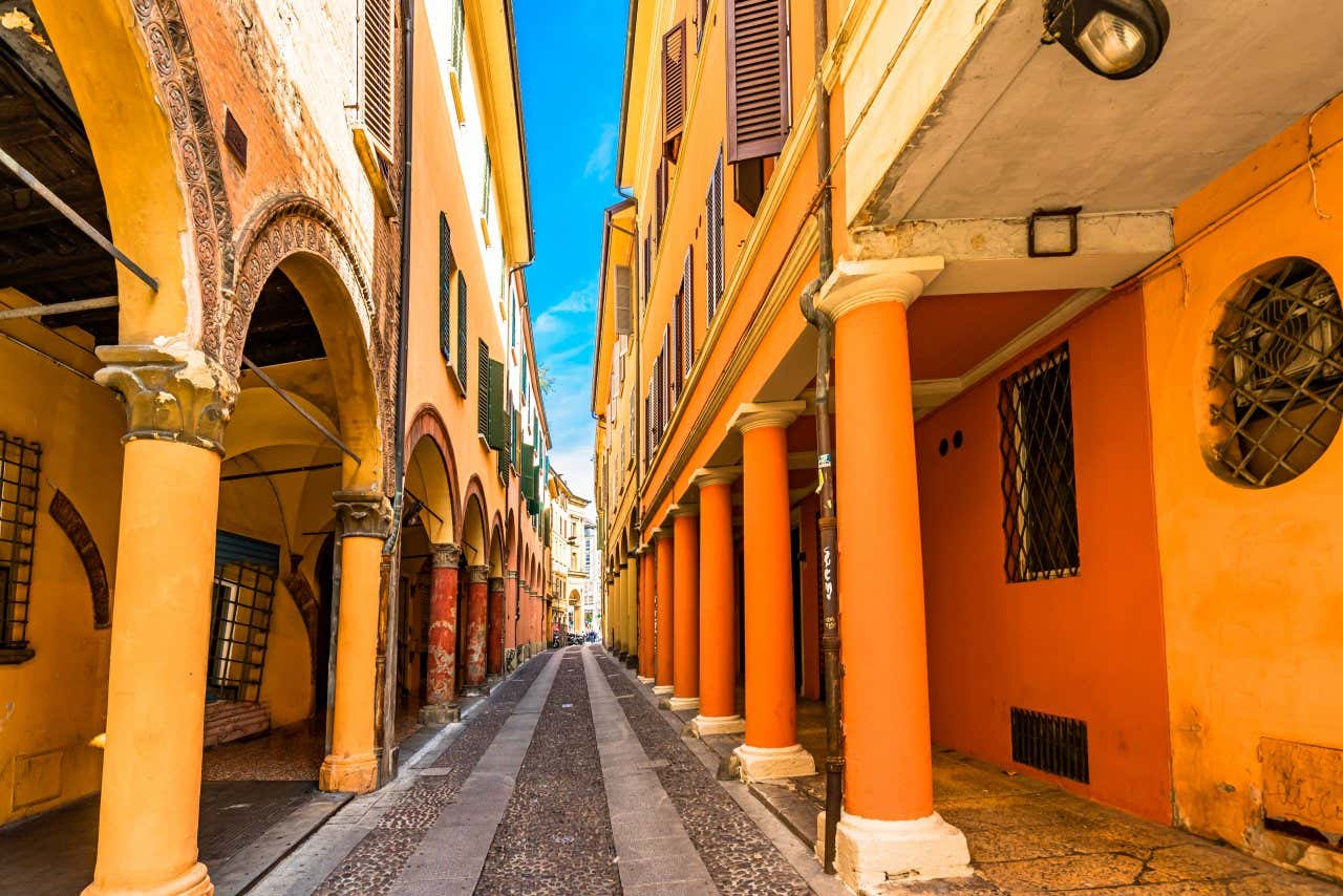 Una estrecha calle del centro de Bolonia con sus característicos pórticos y sus típicos edificios históricos de color rojo anaranjado