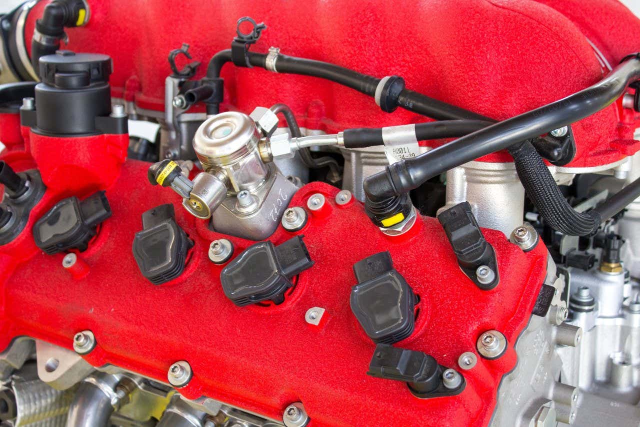 Dettagli di un motore di un'auto Ferrari con manopole e tubi di colore rosso