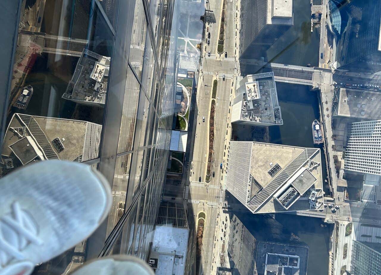 Pés na sacada de vidro com a cidade de Chicago a uma distância de 400 metros