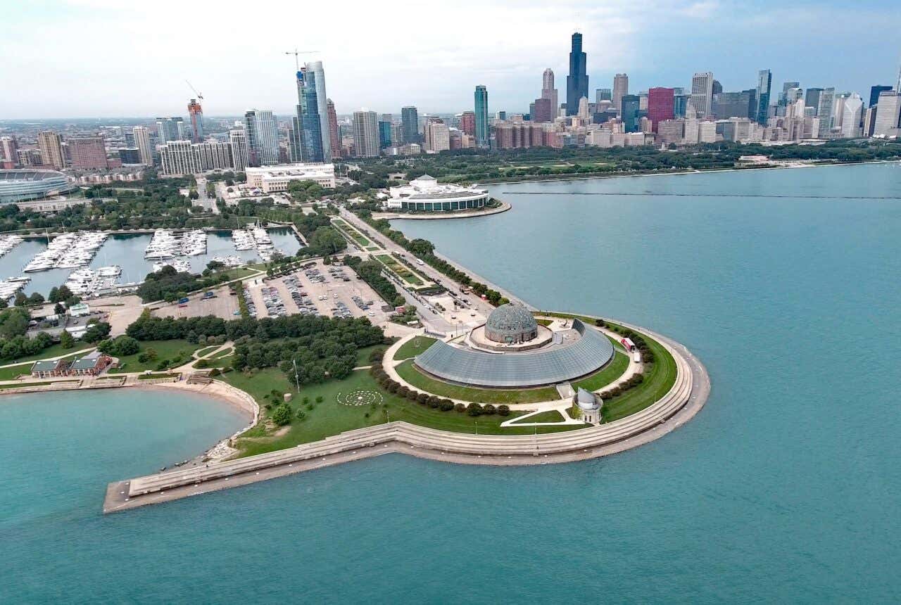 Vista aérea do Museum Campus, com o planetário Adler, o Shedd Aquarium e o Museu Field e o skyline de Chicago ao fundo