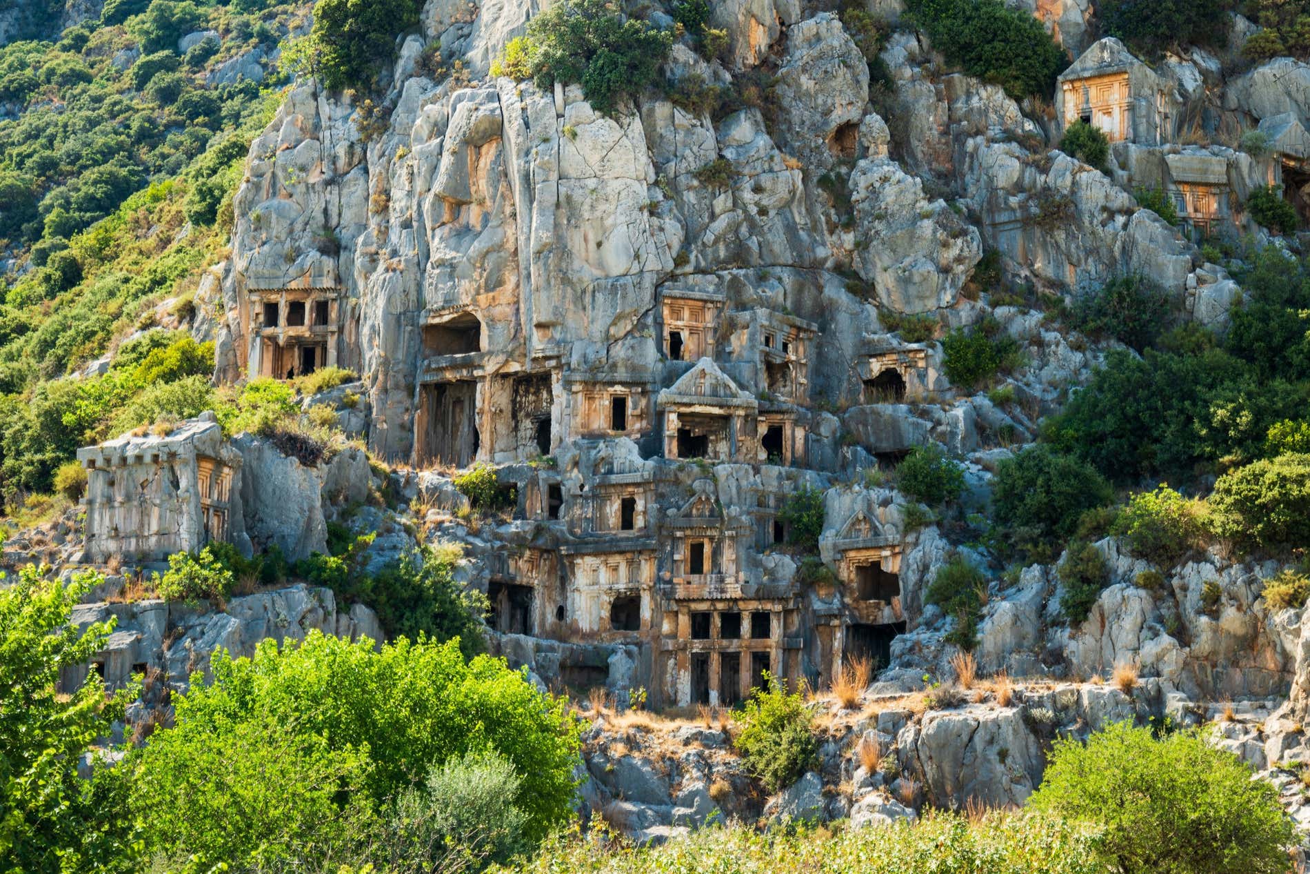 Edifici scavati nella montagna a Demre, in Turchia, circondati dalla vegetazione.