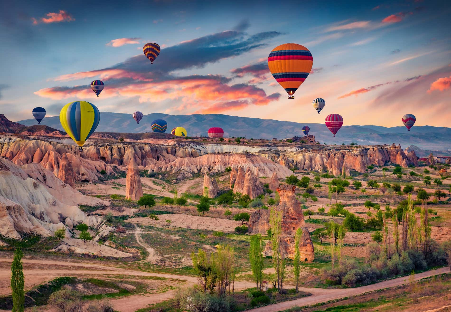Un vasto paesaggio in Cappadocia, con mongolfiere ovunque e le luci dell'alba sullo sfondo.