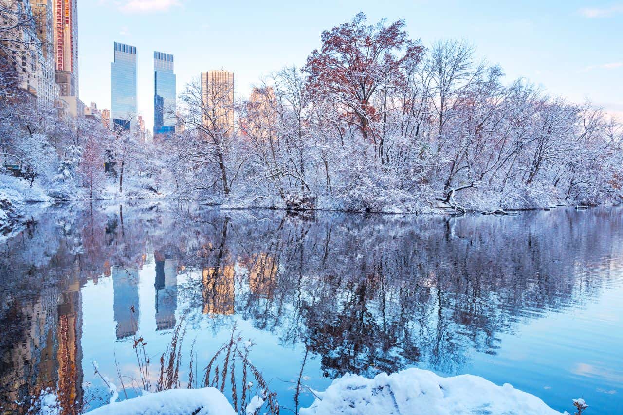 Vue sur un lac de Central Park, à New York, sous la neige, avec des buildings en arrière-plan