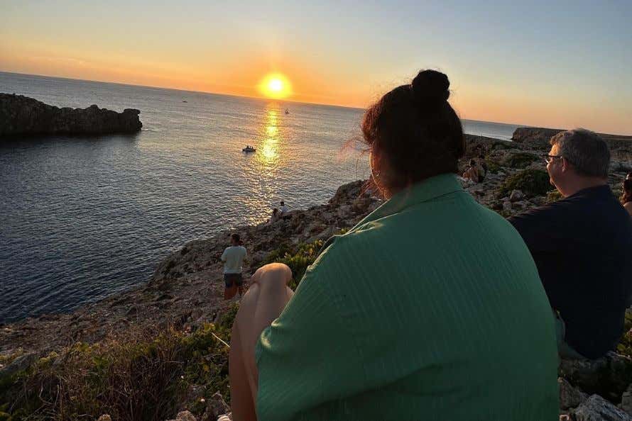 Noelia sentada en las montañas de la costa de Menorca en la puesta del sol