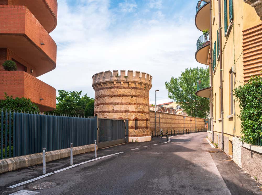 Resti di una torre di vedetta e di mura di cinta medievali incastonate tra la strada asfaltata e i moderni palazzi residenziali di un quartiere di Verona
