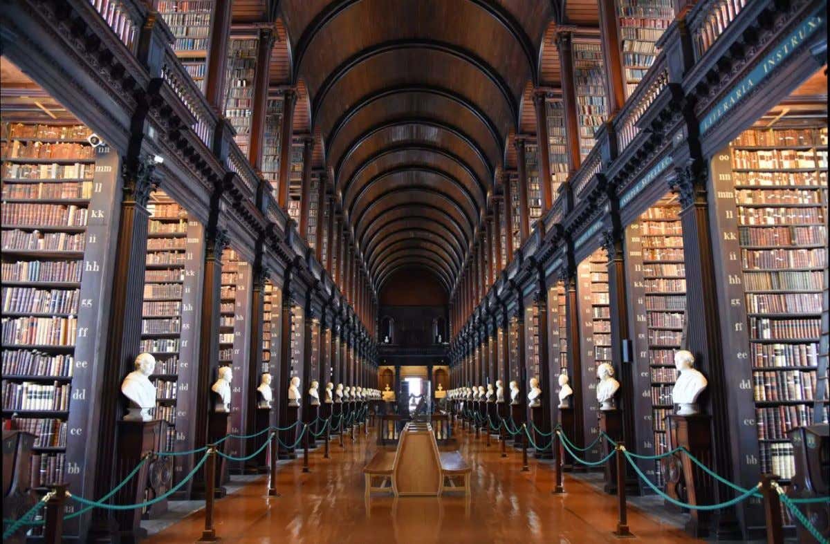 Long Room da Biblioteca do Trinity College com diversos corredores de livros e teto abobadado de madeira