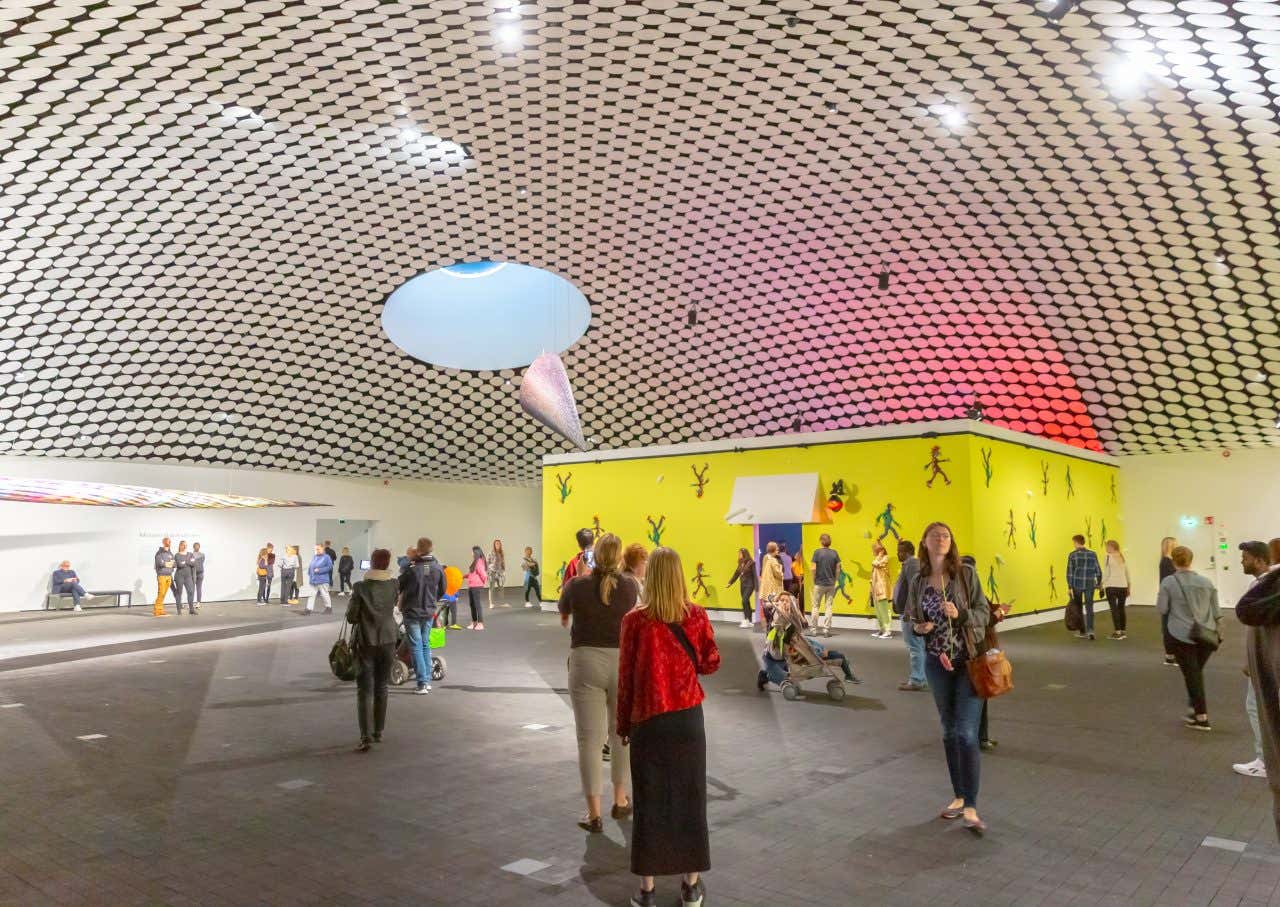 A large domed room in the Kiasma Museum of Contemporary Art, with a black and white roof and lots of people inside.