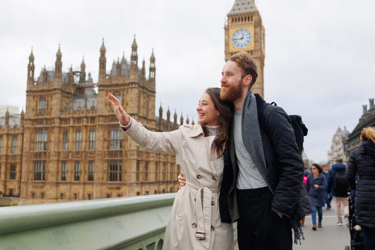 Un hombre y una mujer pasean por un puente, con la torre del Big Ben de Londres de fondo